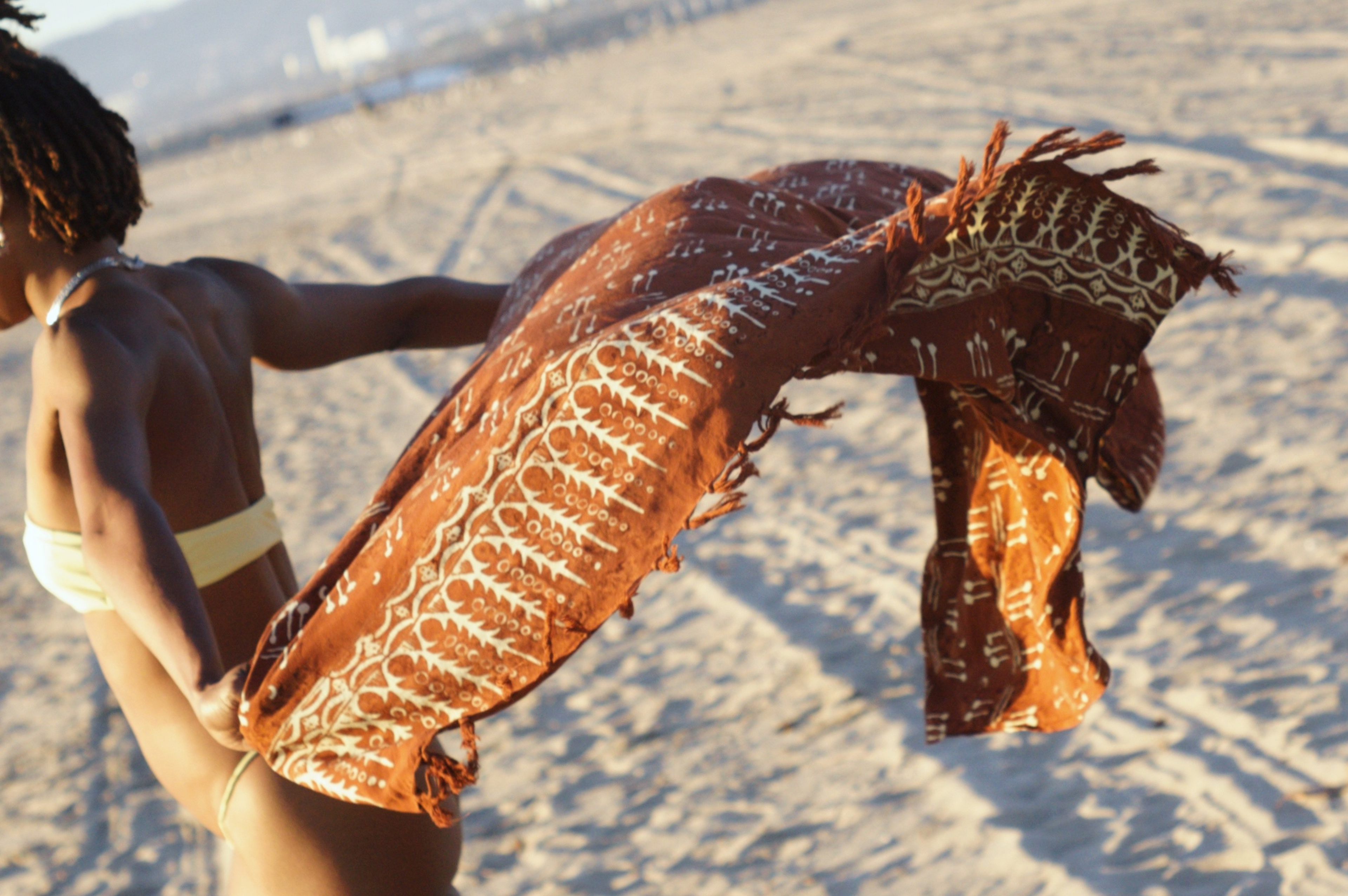A woman holds the Hin Kong Bay - Brown sarong from YUMI & KORA at the beach. Our sarongs can be used as a beach towel or a shawl
