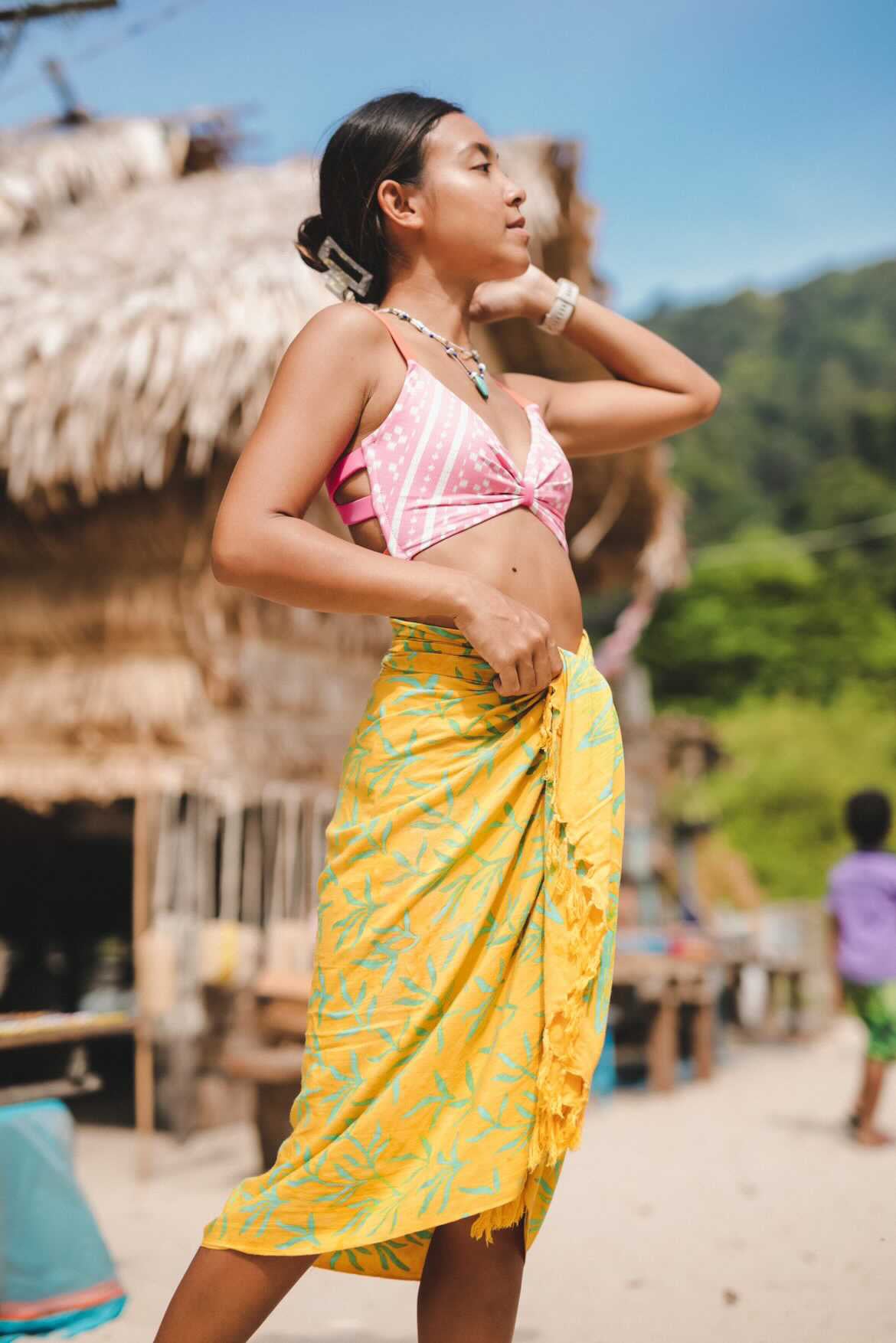 A woman wears the Lanta Reef - Yellow sarong from YUMI & KORA as a swimsuit cover-up skirt at the beach