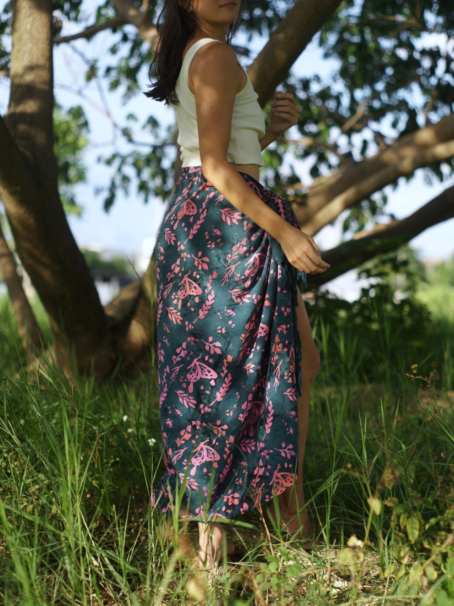 A woman wears the Butterfly - Dark Slate sarong from YUMI & KORA as a skirt. Our sarongs can be tied into a sarong skirt or a sarong dress. Our sarongs work great as a swimsuit coverup