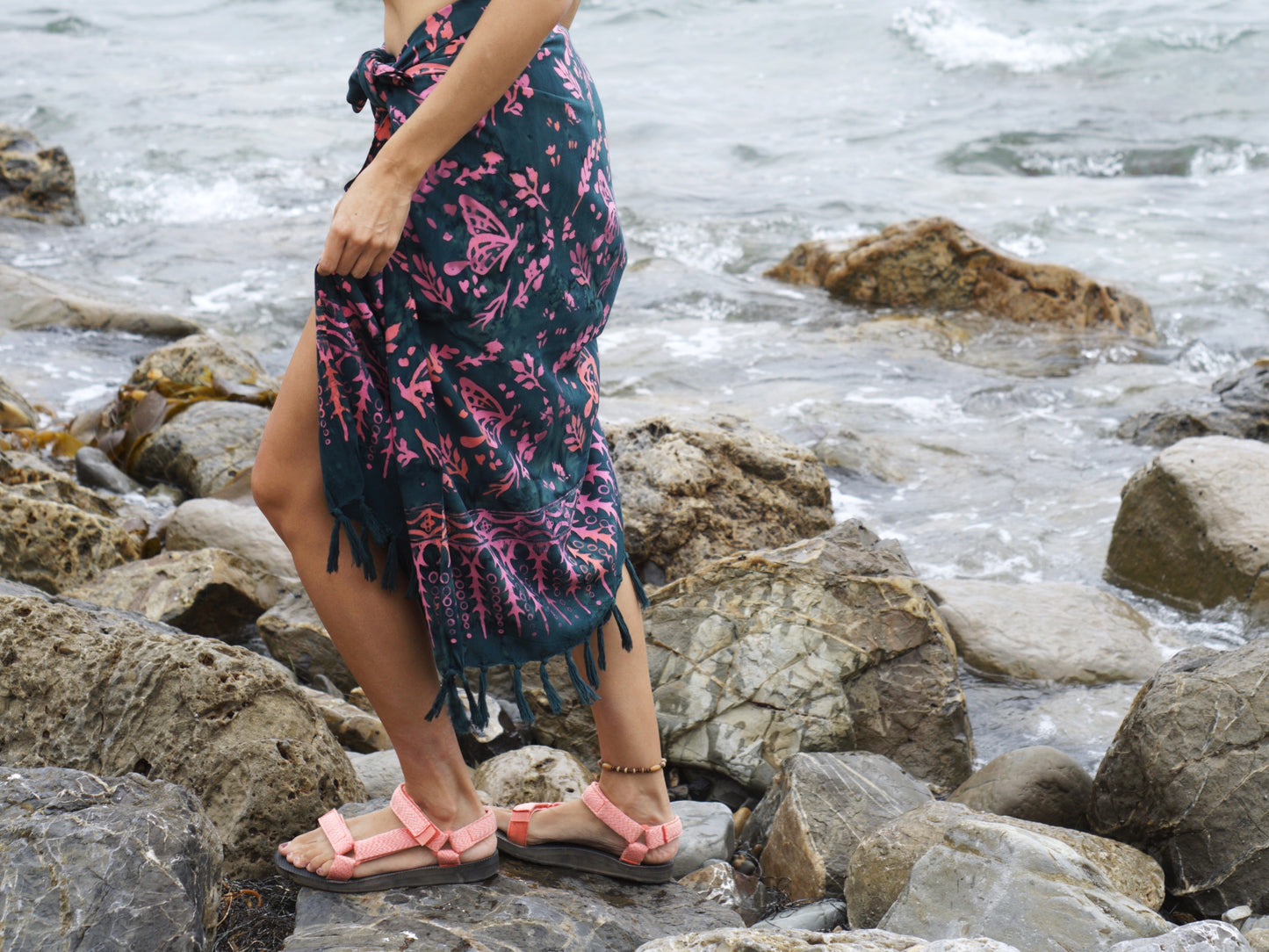 A woman wears the Butterfly - Dark Slate sarong from YUMI & KORA as a skirt. Our sarongs can be tied into a sarong skirt or a sarong dress. Our sarongs work great as a swimsuit coverup