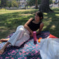 The Butterfly - Dark Slate sarong from YUMI & KORA is used as a picnic blanket at the park. A woman lays on top of the sarong