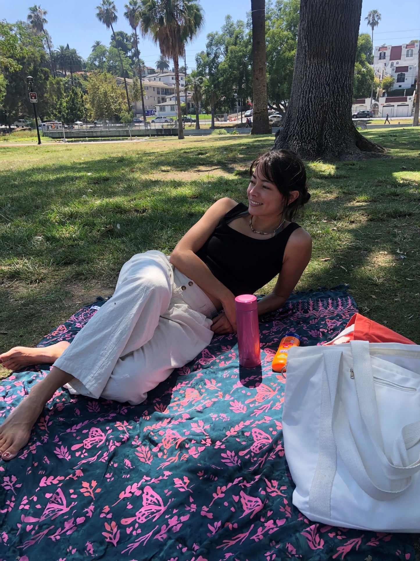 The Butterfly - Dark Slate sarong from YUMI & KORA is used as a picnic blanket at the park. A woman lays on top of the sarong