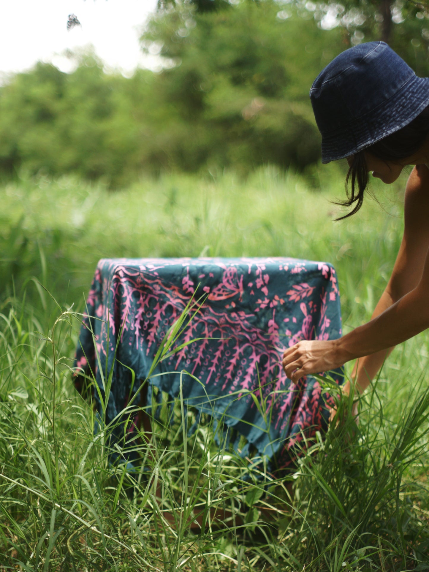 The Butterfly - Dark Slate sarong from YUMI & KORA is used as a tablecloth. A woman adjusts the sarong on a small table