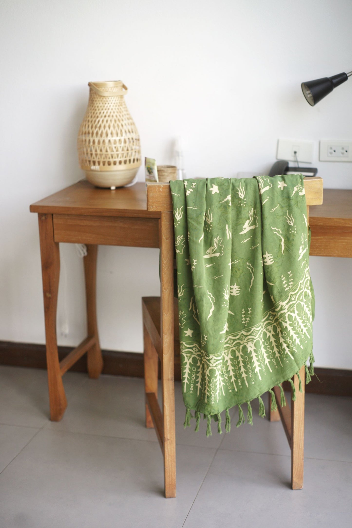 The Duck Dive - Olive Green sarong from YUMI & KORA is draped over the back of a wooden chair. Our sarongs can be used as a tablecloth or as a curtain. They add a splash of color to any room