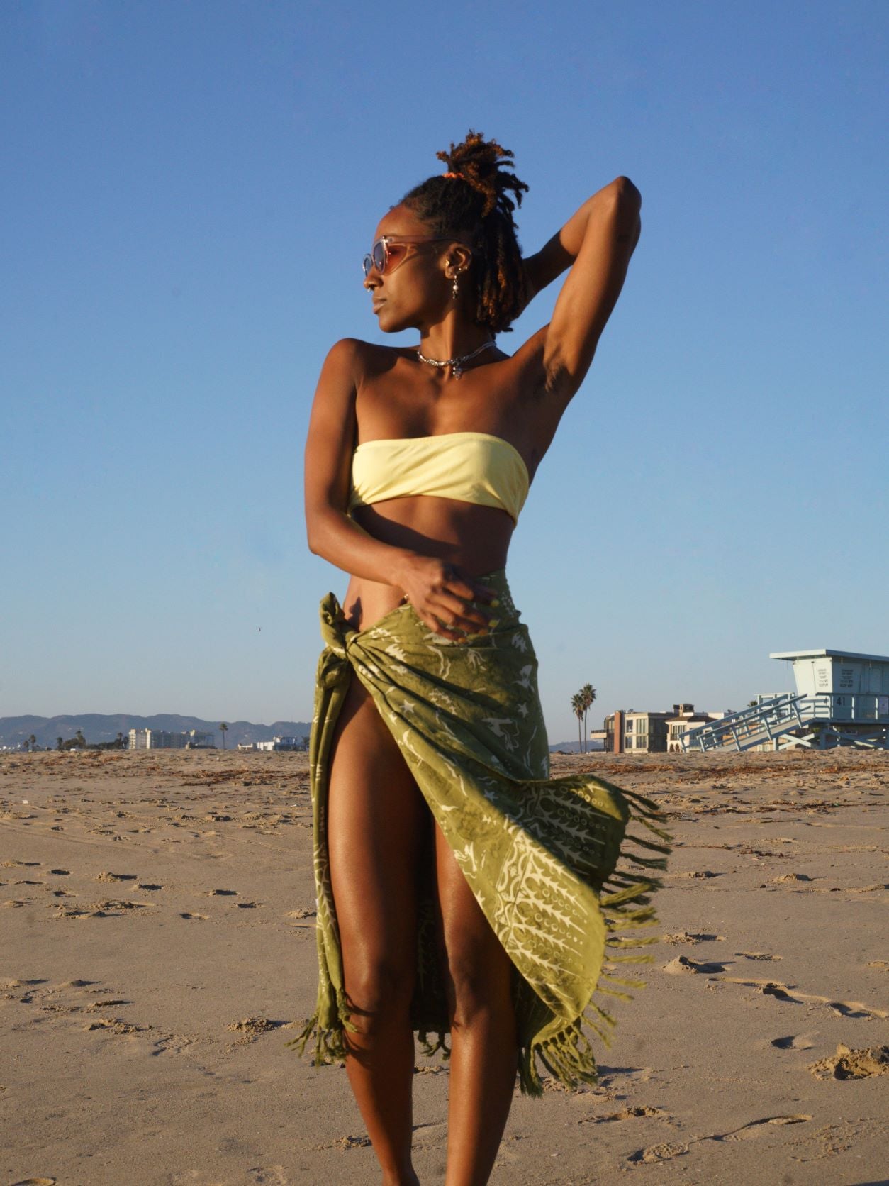 A woman wears the Duck Dive - Olive Green sarong from YUMI & KORA as a swimsuit cover-up skirt. Our sarongs can be tied as a skirt, a dress, or a beach kimono