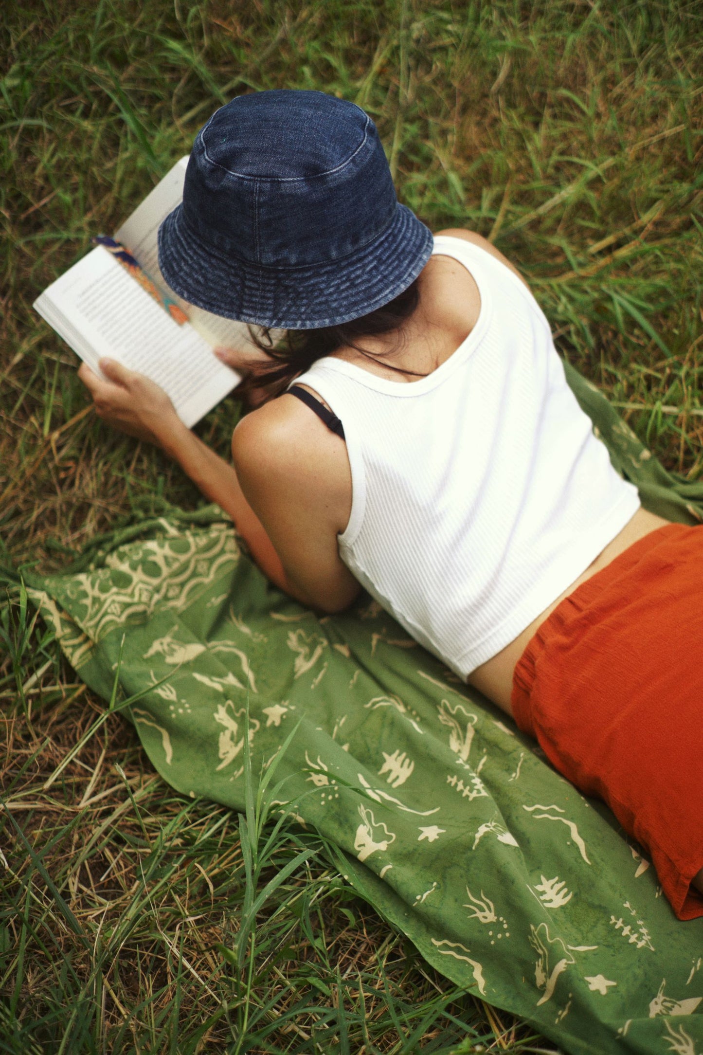 A woman lays on the Duck Dive - Olive Green sarong from YUMI & KORA. Our sarongs can be used as a picnic blanket or a beach towel