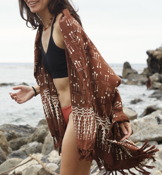 A woman wears the Hin Kong Bay - Brown sarong from YUMI & KORA as a shawl over her swimsuit. Our sarongs can be used as a shawl or a scarf on chilly summer days and nights