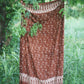 The Hin Kong Bay - Brown sarong from YUMI & KORA hangs from a tree in a meadow. Our sarongs can be used as a home tapestry or as a curtain in your home