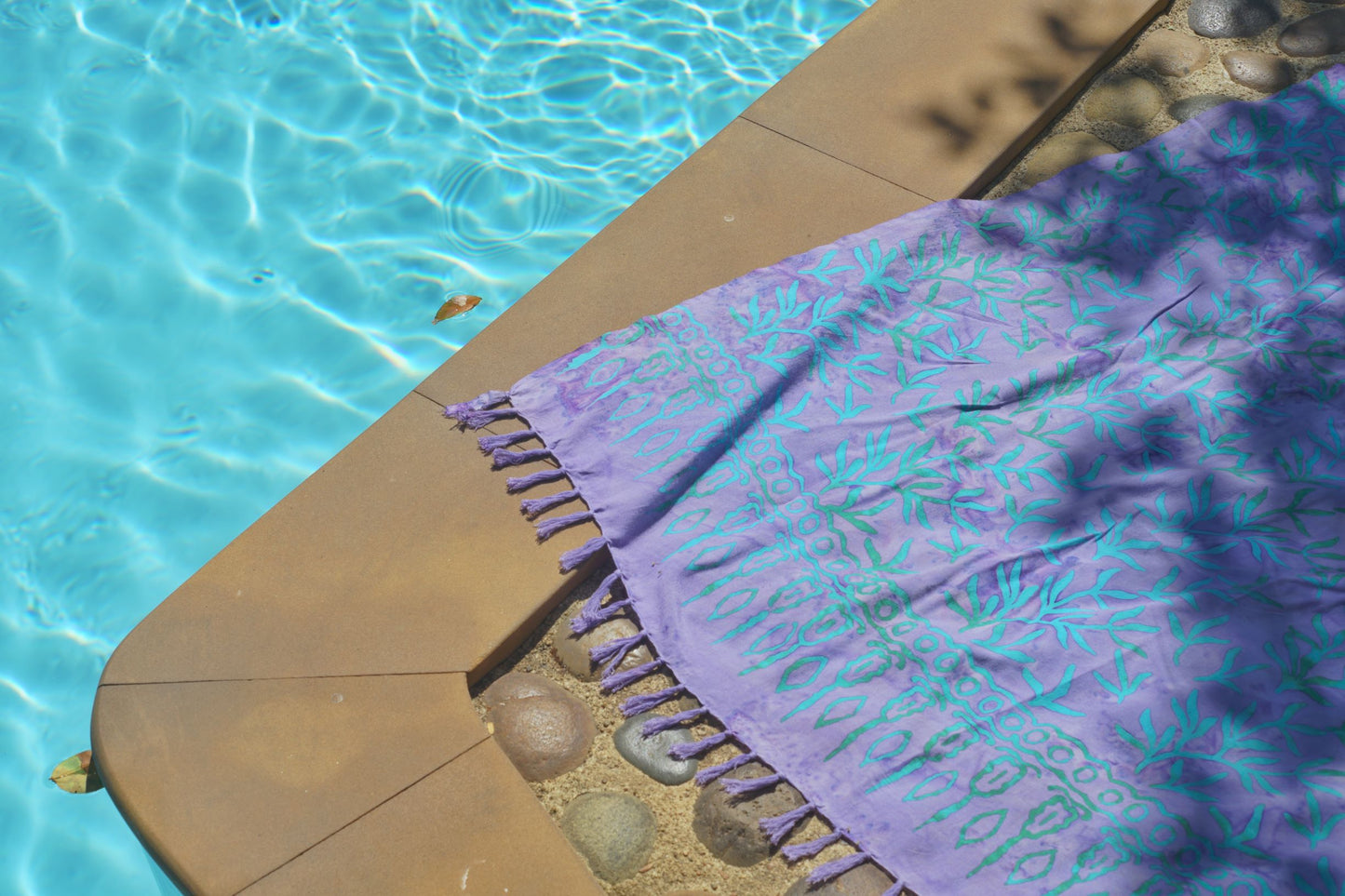 The Lanta Reef - Lavender sarong from YUMI & KORA sits on the ground by the pool as a pool towel