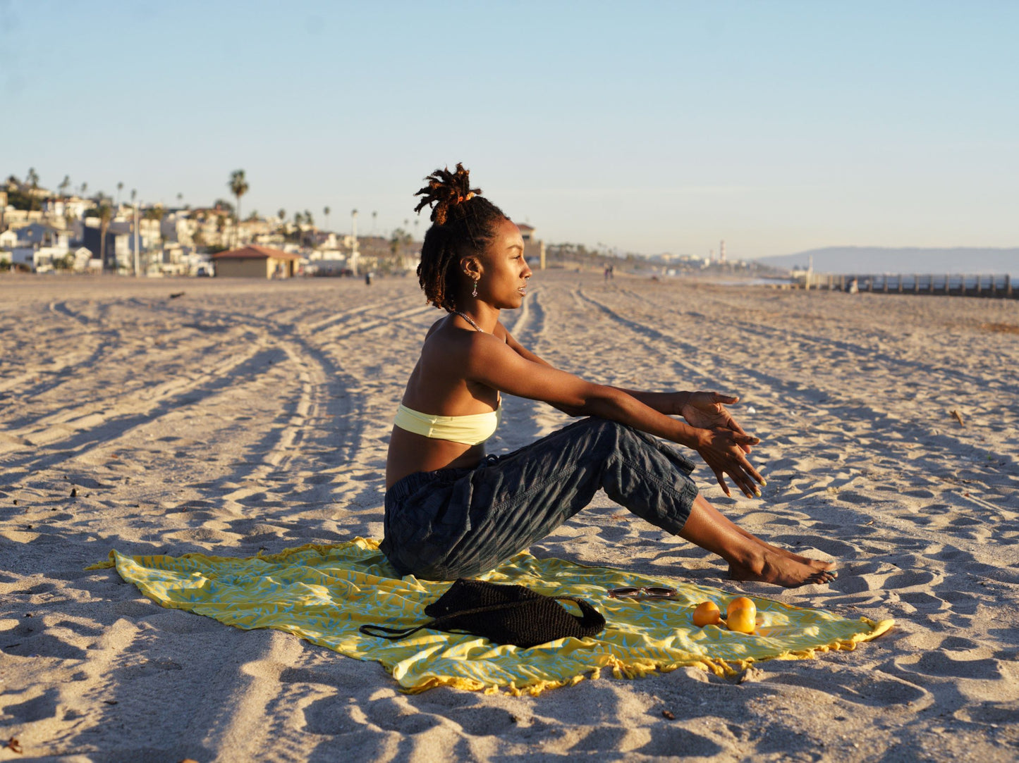 The Lanta Reef - Yellow sarong from YUMI & KORA is used as a beach towel. A woman sits on top of the sarong at the beach