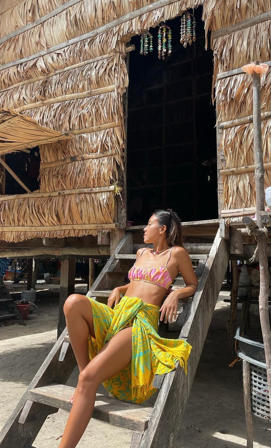 A woman wears the Lanta Reef - Yellow sarong from YUMI & KORA as a swimsuit cover-up skirt at the beach