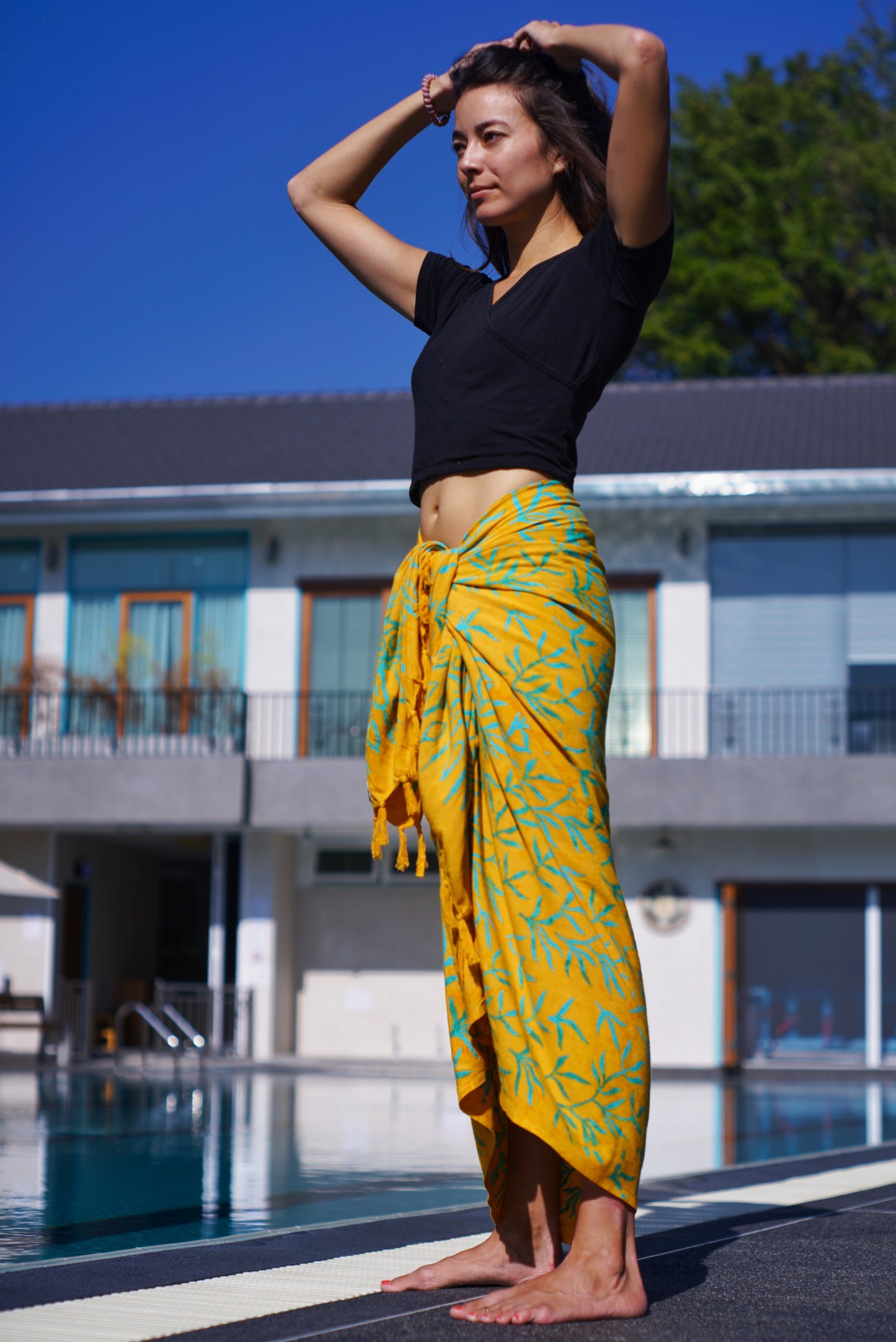 Woman wearing the Lanta Reef - Yellow sarong from YUMI & KORA as a wrap skirt or swimsuit cover up at the pool