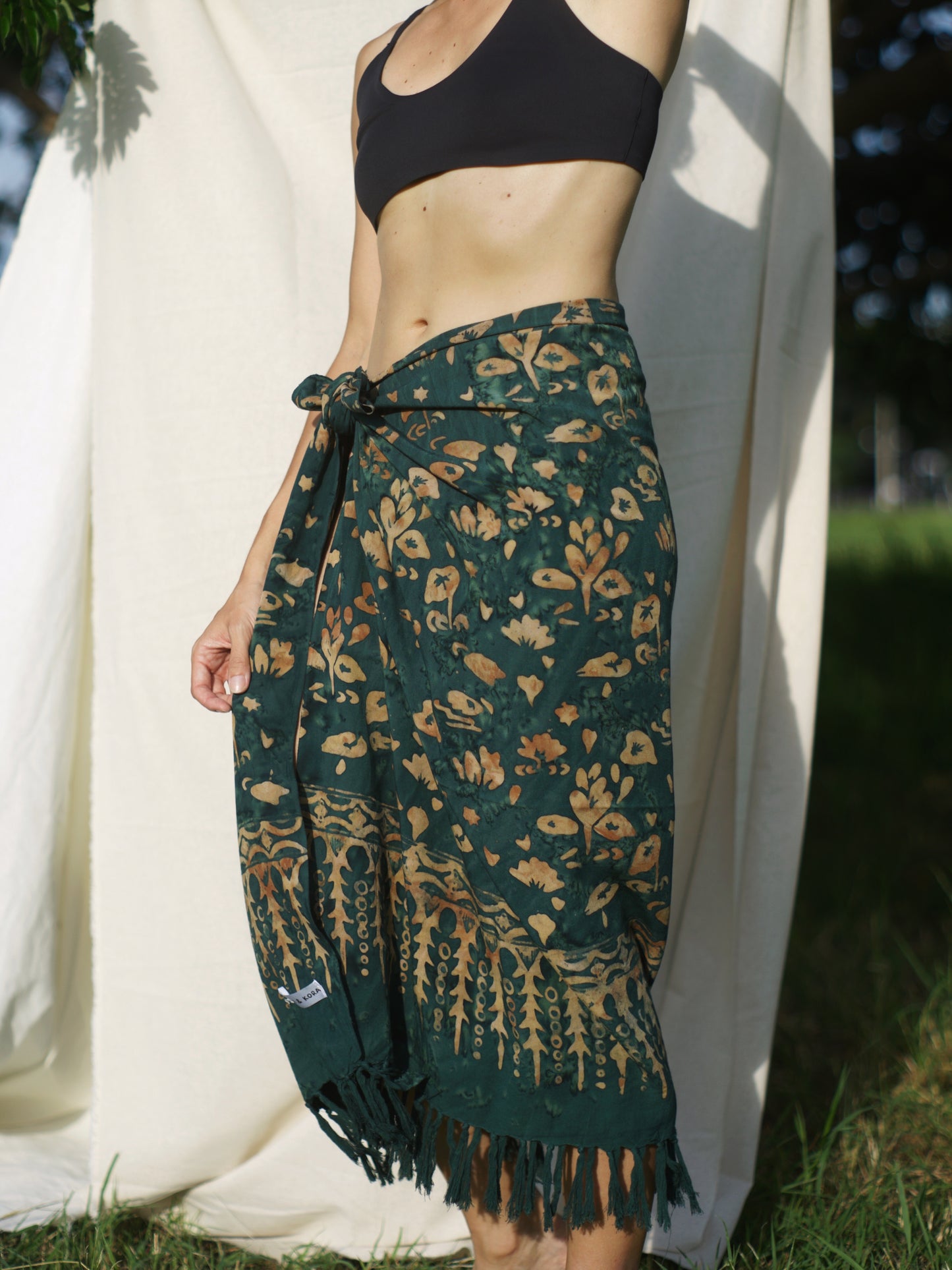 A woman wears the Lily & Lotus - Forest Green sarong from YUMI & KORA as a skirt. Our sarongs can be tied into a sarong skirt or a sarong dress. Our sarongs work great as a swimsuit coverup