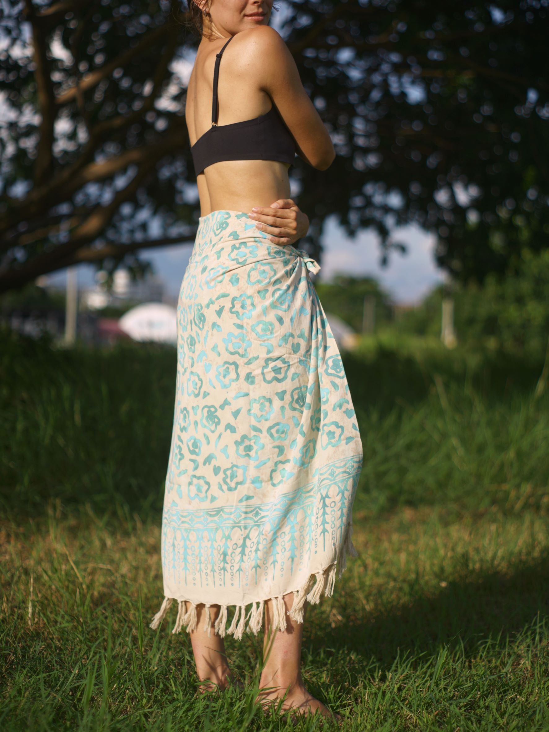 A woman wears the Summer Bloom - Ivory sarong from YUMI & KORA as a skirt. Our sarongs can be tied into a sarong skirt or a sarong dress. Our sarongs work great as a swimsuit coverup