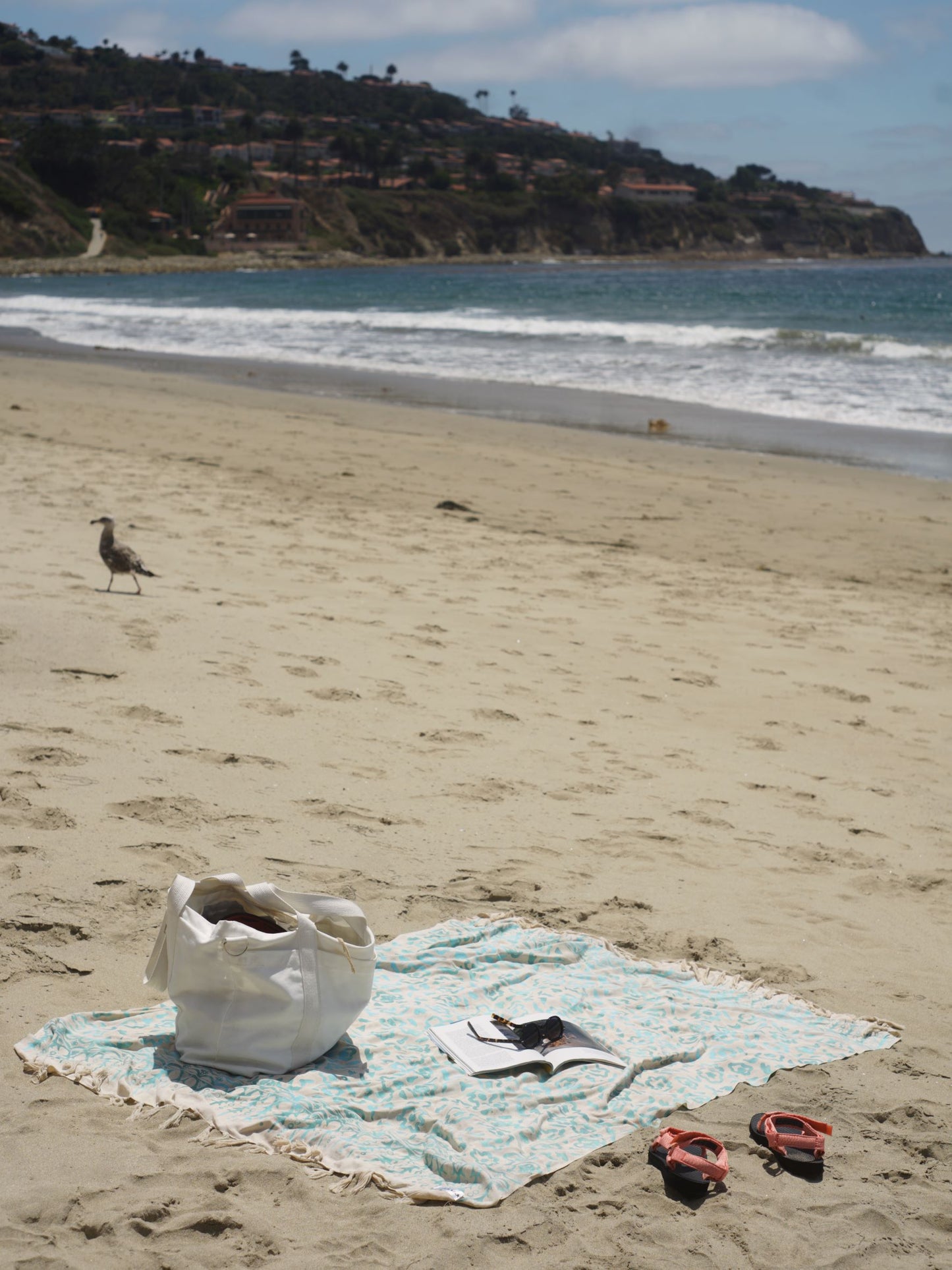 The Summer Bloom - Ivory sarong from YUMI & KORA sits on the sand by the beach. Our sarongs can be used as a beach towel or as a pool towel