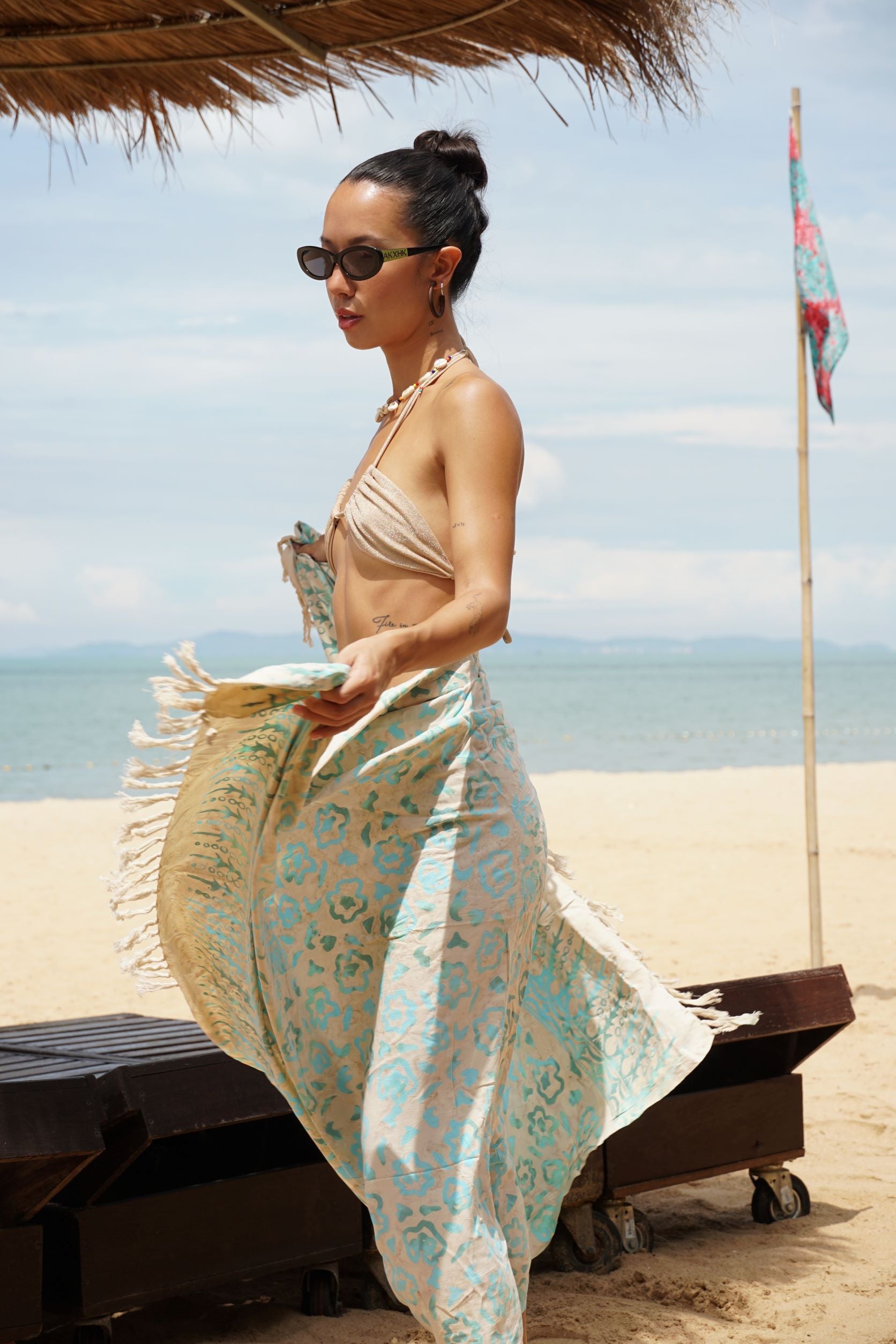 A woman wraps the Summer Bloom - Ivory sarong from YUMI & KORA around her body at the beach. Our sarongs can be tied into a skirt, a dress, or a beach kimono