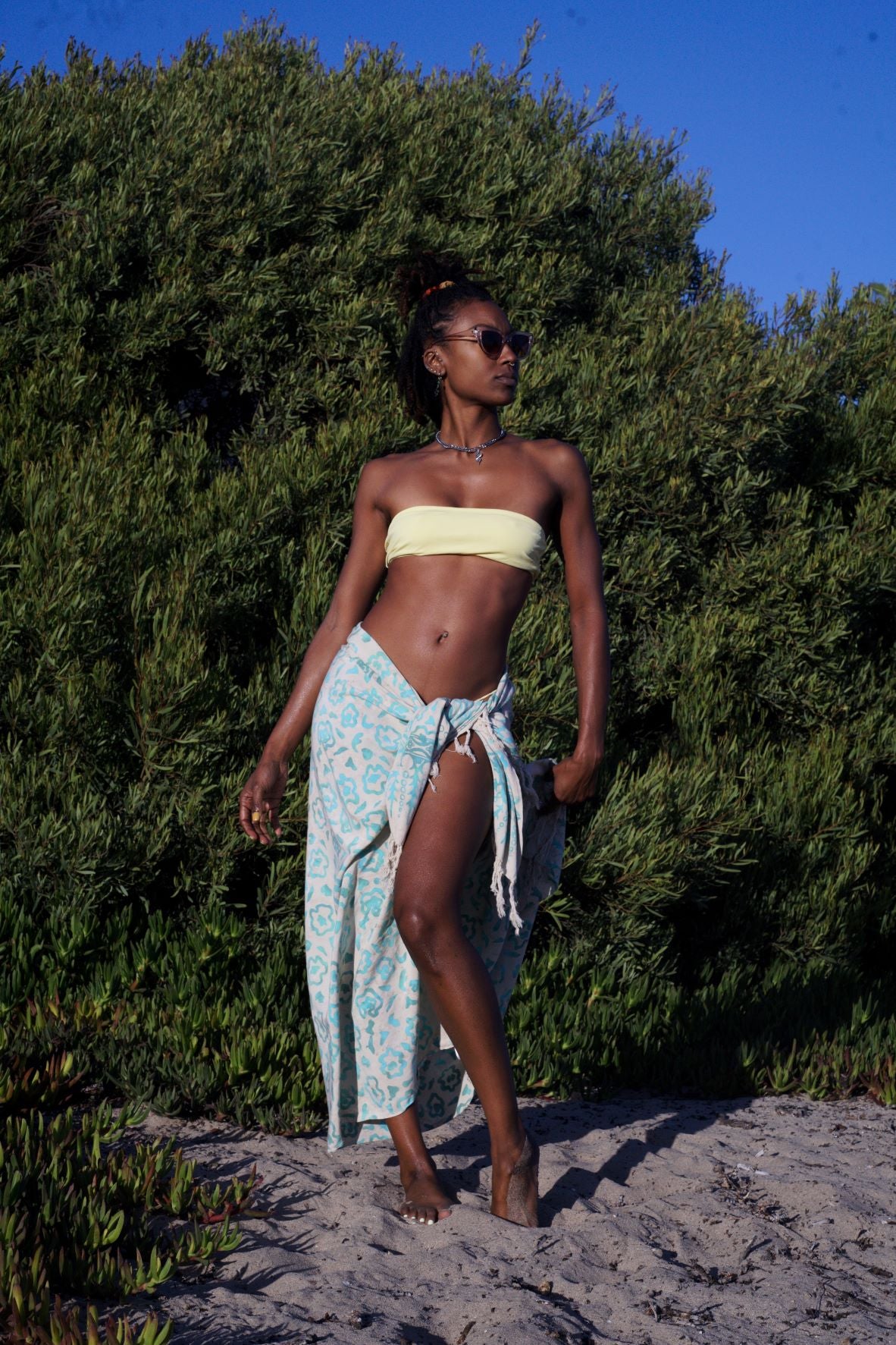 A woman wears the Summer Bloom - Ivory sarong from YUMI & KORA as a swimsuit cover-up skirt. Our sarongs can be tied into a skirt, a dress, or a beach kimono