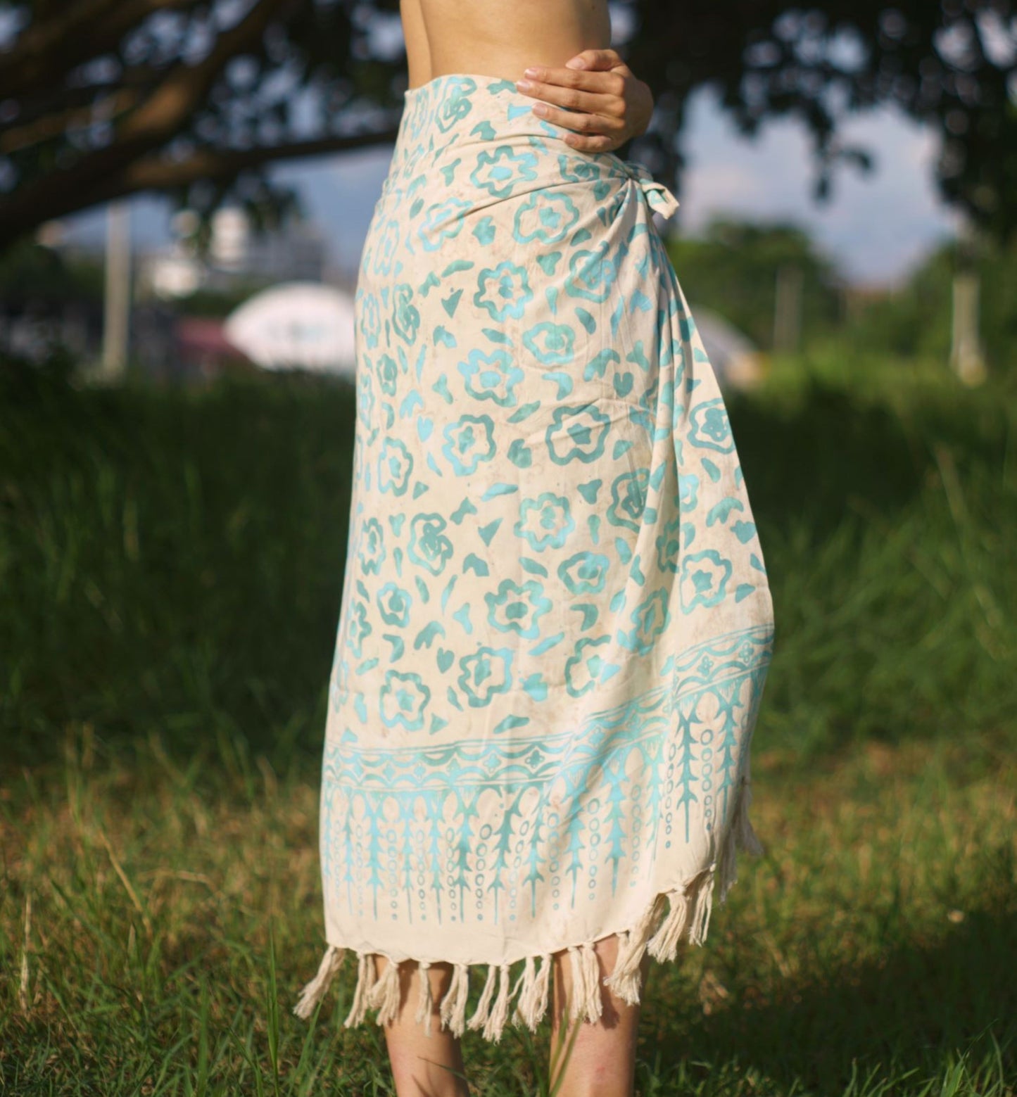 A woman wears the Summer Bloom - Ivory sarong from YUMI & KORA as a skirt. Our sarongs can be tied into a sarong skirt or a sarong dress. Our sarongs work great as a swimsuit coverup