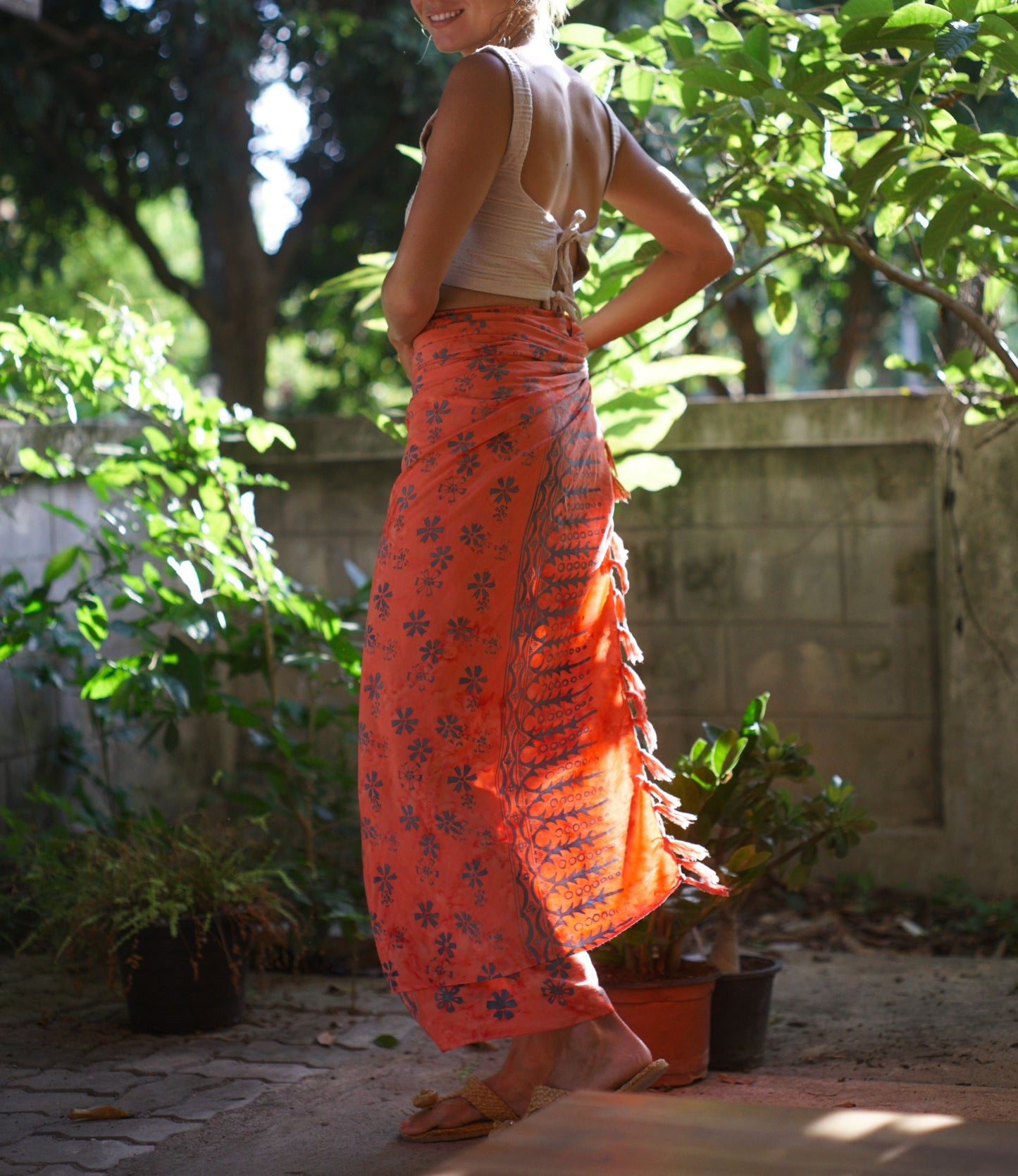 A woman wears the Sweet Cosmos - Pink sarong from YUMI & KORA as a skirt, paired with a white crop top