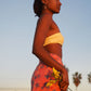 A woman wears the Sweet Cosmos - Pink sarong from YUMI & KORA as a swimsuit cover-up skirt at the beach. Our sarongs can be tied as a skirt, a dress, or a beach kimono