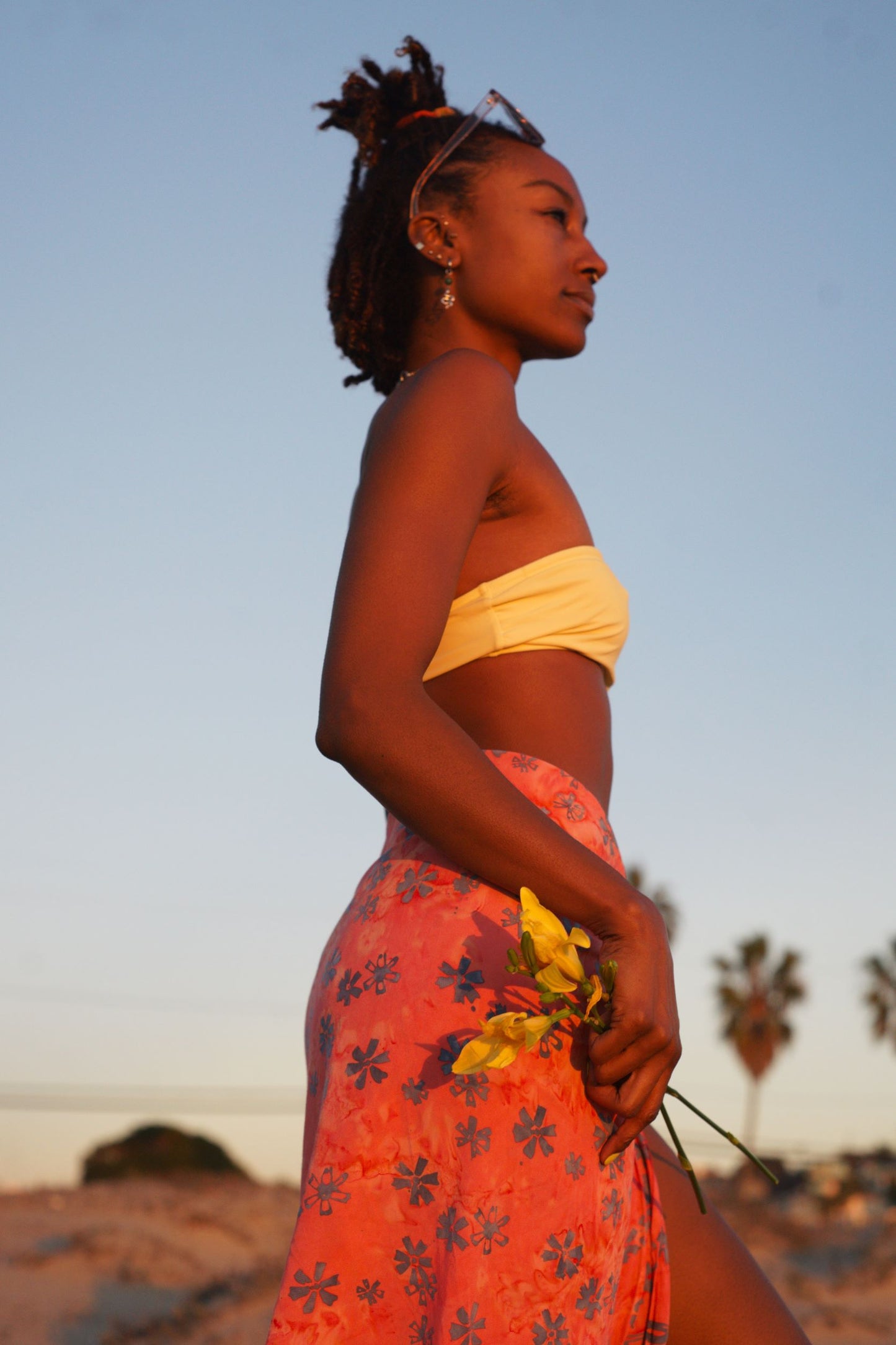 A woman wears the Sweet Cosmos - Pink sarong from YUMI & KORA as a swimsuit cover-up skirt at the beach. Our sarongs can be tied as a skirt, a dress, or a beach kimono