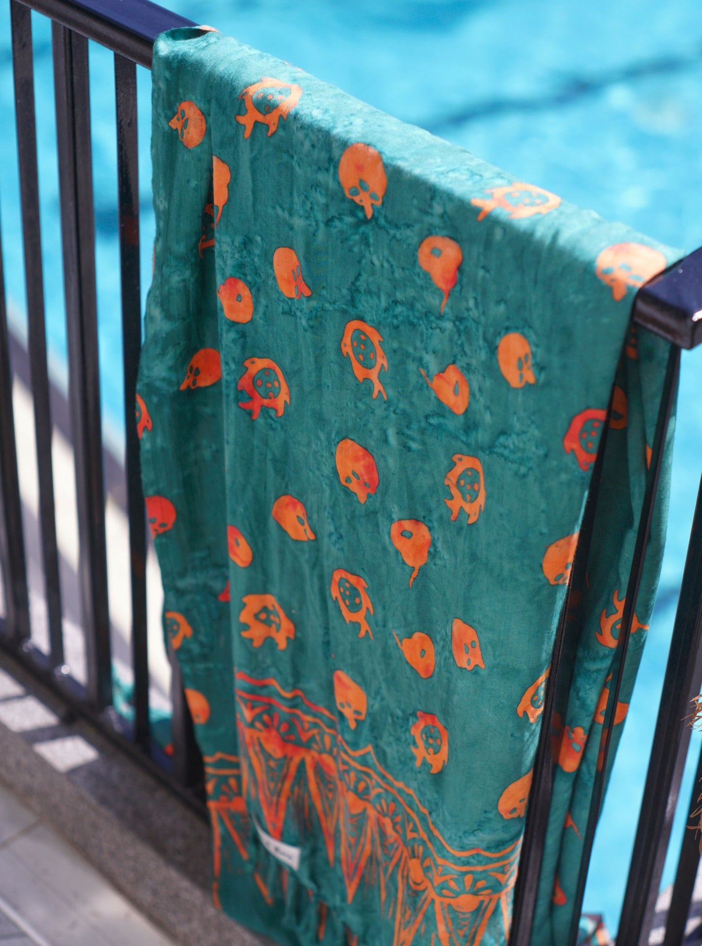 The Tropical Dream - Teal sarong from YUMI & KORA is hanging on a rail by the pool